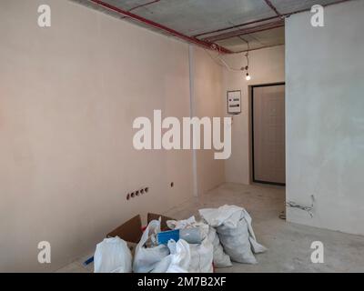 Weiße Polypropylenbeutel gefüllt mit Bauschutt in der Wohnung. Polypropylenbeutel. Bauabfälle. Reparatur im Zimmer. Industrieabfälle Stockfoto