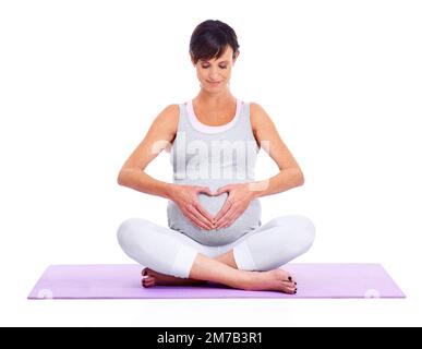 Ruhe und Gelassenheit für Mutter und Baby. Eine junge werdende Mutter meditiert friedlich, während sie auf Weiß isoliert ist. Stockfoto