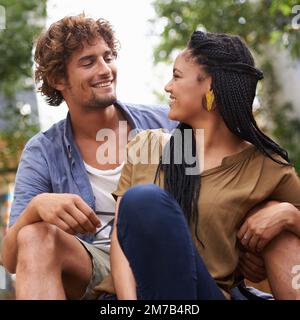 In den Augen des anderen verloren. Ein liebevolles junges Paar, das draußen sitzt. Stockfoto