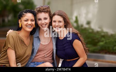 Zeit zusammen ist einfach nie genug. Drei schöne junge Frauen, die fröhlich lächeln, während sie draußen sitzen. Stockfoto