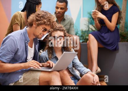 Chillen auf dem Campus zwischen den Klassen. Eine Aufnahme von Studenten, die auf dem Campus einen Laptop teilen. Stockfoto