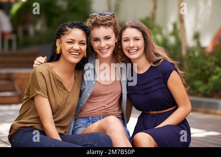 Freundschaft ist keine große Sache, es sind eine Million kleiner Dinge. Ein Porträt von drei jungen Freunden, die fröhlich lächeln, während sie draußen sitzen. Stockfoto