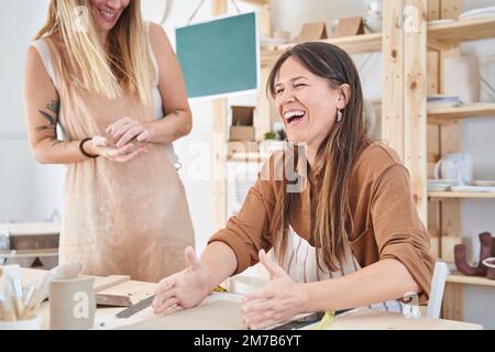 Eine Frau, die einer Schülerin mit Kunsthandwerk in einem Töpferkurs hilft. Handwerk, Kunst und Hobbys. Stockfoto
