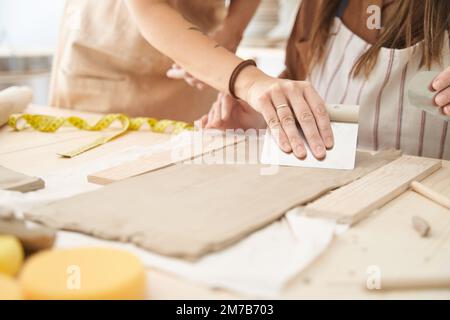 Freunde mit Schürzen in einer Töpferwerkstatt bereiten Ton vor, um Stücke zu kreieren. Handwerksklasse. Stockfoto