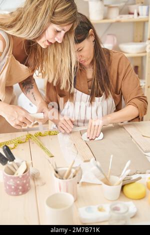 Freunde mit Schürzen in einer Töpferwerkstatt bereiten Ton vor, um Stücke zu kreieren. Handwerksklasse. Stockfoto