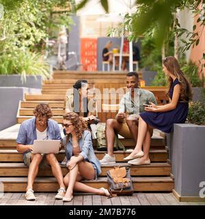 Zwischen den Kursen auf dem Campus chillen. Eine Gruppe junger Freunde, die während einer Pause ihre Laptops und Handys benutzen. Stockfoto