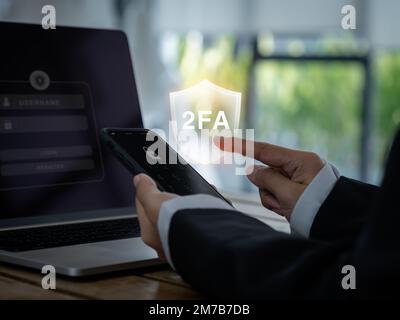 Zweistufiges Authentifizierungskonzept. 2FA in Schild-Symbol wird auf dem Smartphone angezeigt, während Geschäftsmann auf Kennwort drückt, um eine Verbindung mit dem Laptop-Computer herzustellen, ID Stockfoto