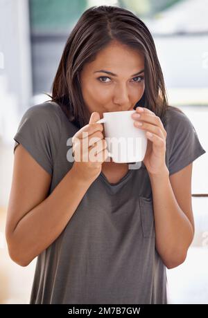 Beginnen Sie den Tag mit einer frischen Tasse... eine attraktive junge Frau steht in ihrer Küche, während sie Kaffee trinkt. Stockfoto