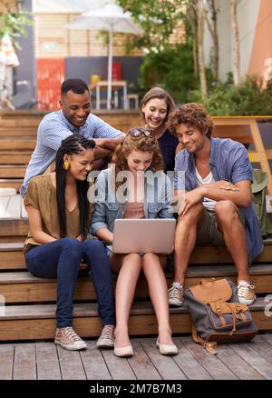 Wir wollen diese Lektion online durchgehen. Eine Gruppe von Schülern versammelte sich im Freien um ein Notebook. Stockfoto