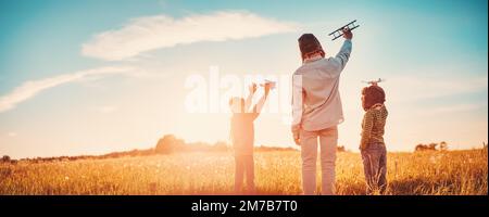 Vater und seine Kinder spielten mit dem Spielzeug des Flugzeugs auf dem Abendfeld. Stockfoto