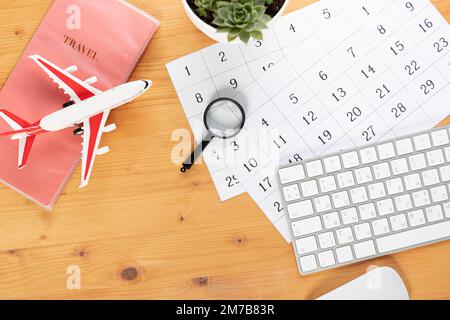 Kalender und Erinnerungen für Geschäftsreisen, Reisen und Urlaub. Gleiter auf dem Schreibtisch mit Flugzeug und Lupe, Stift und Tastatur. Markierung wichtig Stockfoto