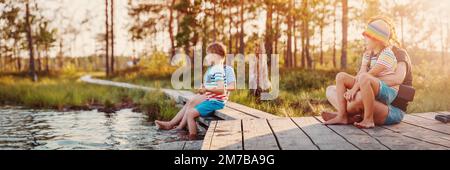 Mutter mit ihren Kindern, die am Pier des Sumpfsees saßen. Stockfoto