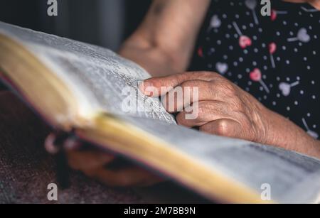 Eine alte Frau liest die Bibel, die Hände sind dicht. Stockfoto