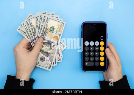 Geld und einen Taschenrechner in männlichen Händen auf blauem Hintergrund, Draufsicht. Stockfoto