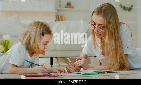 Kleine Adoptivkinder zeichnen gern Kunst mit weißer Mutter in Gläsern, die zusammen auf dem Hausboden liegen. Tochter Baby Kind mit Mami mom Stockfoto