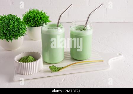 Zwei moderne Gläser in Form einer Bierdose mit Eistee-Matcha mit Stroh auf einem Brett an einer Ziegelwand. Eine Alternative zum Kaffee. Koffein Stockfoto