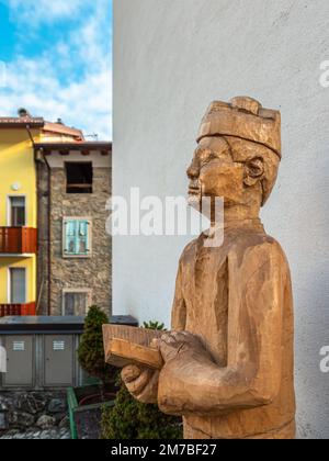 Sutrio, Italien - 29. Dezember 2022: Eine hölzerne Skulptur eines Dorfpastors mit einem offenen Buch Stockfoto