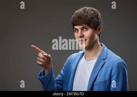 Junger Mann in Jacke zeigt auf Kopierraum Stockfoto
