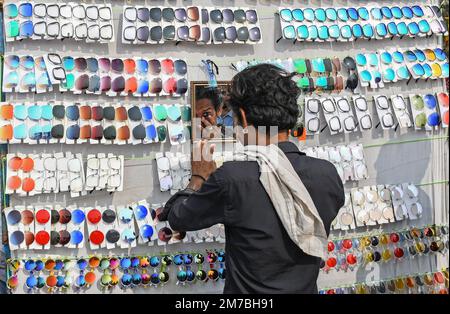 Mumbai, Indien. 08. Januar 2023. Während der Erangal-Messe in Mumbai blickt ein Straßenhändler, der Sonnenbrillen verkauft, in den Spiegel. Die Messe ist auch bekannt als St. Bonaventure Festmahl. Es markiert die Taufe oder Namenszeremonie von Jesus Christus und ist wie ein jährliches Treffen der ostindischen Gemeinschaft. Die Leute kommen und beten in der St. Bonaventure Kirche, die sich am Strand befindet, posten, dass sie Vergnügungsfahrten am Strand genießen und dort Essen und essen. Kredit: SOPA Images Limited/Alamy Live News Stockfoto