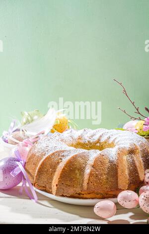 Traditionelle Frühlingsferien Osterrunde Kuchen mit Puderzucker gekrönt. Auf hellem Holzhintergrund mit Sonnenlicht, Ostereiern, Dekor und Frühlingszwirnholz Stockfoto