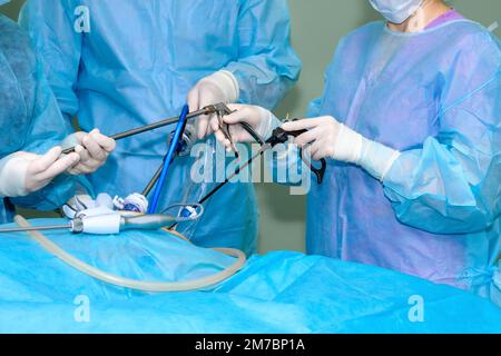 Die Hände des Chirurgen in sterilen Handschuhen benutzen laparoskopische Operationsinstrumente. Ein Team von Chirurgen operiert einen Patienten im Operationssaal. Selektiver Fokus. Stockfoto