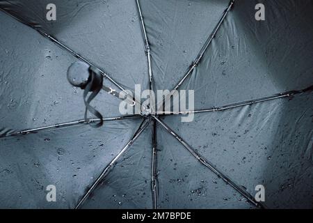 Schwarzer nasser Regenschirm, mit kleinen Wassertropfen von innen, Schirmspeichen. Schlechte Wettervorhersage, Sturm im Herbst oder Frühling. Zubehör für Stockfoto