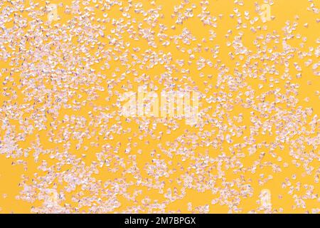 Kleine silberne Kristallkonfetti auf hellgelbem Hintergrund. Glitzernde Textur. Stockfoto