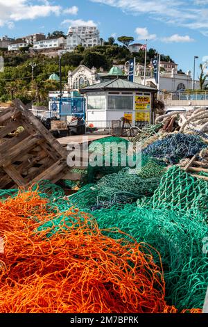 Ein Wirrwarr aus leuchtend orangefarbenen und grünen Fischernetzen im Hafen von Torquay, Devon, Großbritannien. Stockfoto