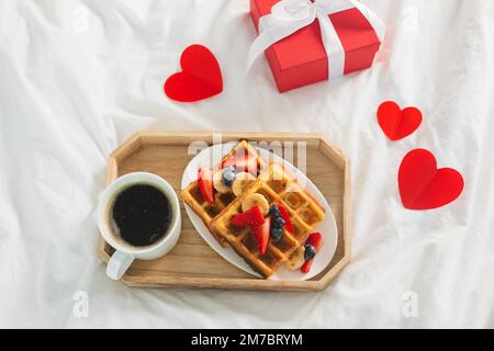 Frühstück am Valentinstag mit Kaffee und belgischen Waffeln auf weißer Bettwäsche. Draufsicht Stockfoto