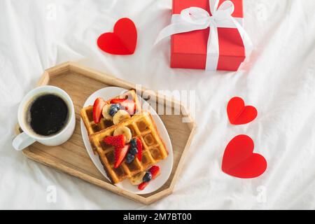 Frühstück am Valentinstag mit Kaffee und belgischen Waffeln auf weißer Bettwäsche. Draufsicht Stockfoto