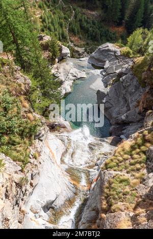 Blick von oben auf den Lillaz-Wasserfall (Cascate di Lillaz) und den smaragdgrünen Teich darunter, Felsen umgeben von grün-gelber Herbstvegetation Stockfoto