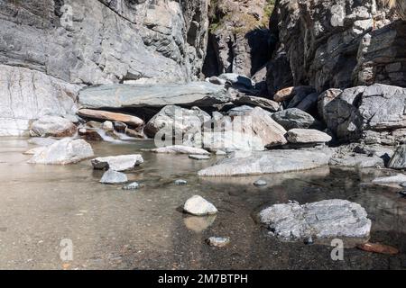 Pfütze mit kristallklarem Wasser und kleinen Kieselsteinen und Sand am Boden, geformt durch den Lillaz-Wasserfall (Cascate di Lillaz) in Granitriss Stockfoto