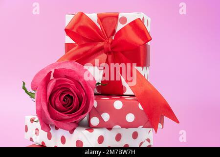 Geschenkschachteln mit Punktmuster übereinander und Schleife und pinkfarbener Rose als Hintergrund. Geburtstag, 14. Februar, Internationaler Frauen- und Muttertag Stockfoto