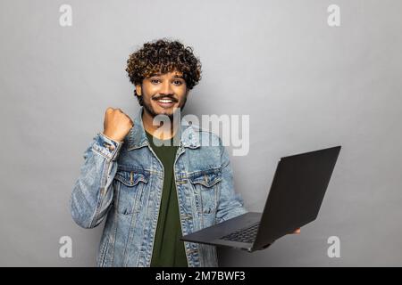 Porträt eines freudigen, bärtigen Geschäftsmanns, der vor Freude schreit und ein Notebook in der Hand hält, sich über den Sieg freut, online wettet, einen offiziellen Anzug trägt. Drinnen Stockfoto