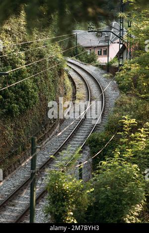 Eisenbahn zum Anheben des Zuges entlang der Schienen, zwischen den grünen Bäumen, vorbei an den Wohngebäuden. Der Zug transportiert Passagiere und bringt sie Stockfoto