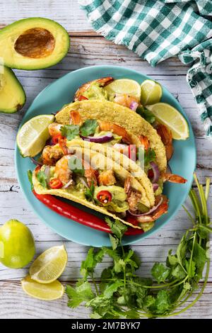 Mexikanische Tacos mit Garnelen, Guacamole und Gemüse auf einem Holztisch Stockfoto