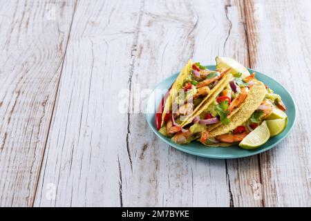 Mexikanische Tacos mit Garnelen, Guacamole und Gemüse auf einem Holztisch Stockfoto