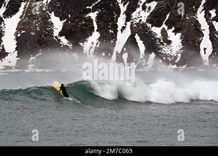Surfer, der sich im Winter am Strand von Ramberg auf der Halbinsel Lofoten im Norden Norwegens auf eine Welle drängt. Stockfoto