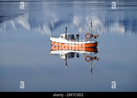 Ein kleines Fischerboot, das in einem Fjord südlich von Alta im Norden Norwegens vor Anker liegt, während sich die Berge im Meer spiegeln. Stockfoto