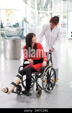 Frau mit einem kurzen Bein im Rollstuhl, die von einer Krankenschwester in Österreich geschoben wird Stockfoto