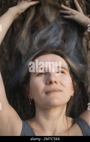 Nahaufnahme einer erwachsenen Frau, die auf Baumrinde liegt und sich ein Himmelsporträt ansieht Stockfoto