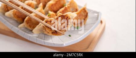 Taiwanesisches und japanisches gebratenes Gyoza-Knödel-Jiaozi-Essen auf einem Teller mit Sojasauce auf weißem Tischhintergrund. Stockfoto