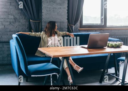 Eine Frau sitzt auf einer Couch im Wohnzimmer und wartet auf ihre Uhr. Stockfoto