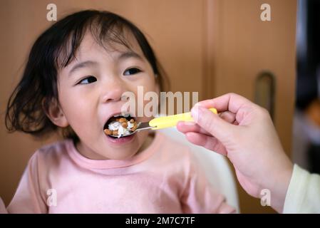 Ein Kleinkind, das Natto isst - eine japanische fermentierte Sojabohnen. Gesundes Essen. Handfütterung Stockfoto