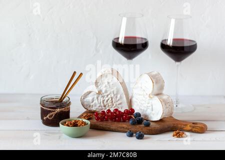 Herzförmiger Käse, serviert mit Beeren und zwei Rotweingläsern, Valentinstag-Konzept, Seitenblick Stockfoto