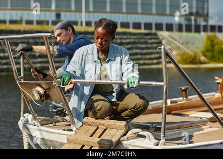 Das ganze Porträt einer schwarzen jungen Frau, die auf einem Boot arbeitet, beleuchtet von Sonnenlicht, Kopierraum Stockfoto