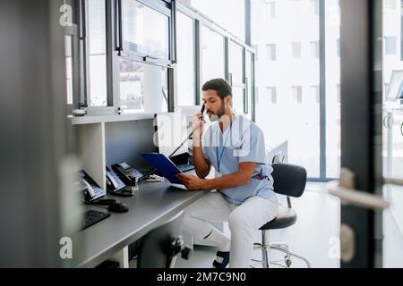 Junger multirassischer Arzt, der an der Rezeption sitzt und anruft. Stockfoto