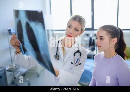 Junge Ärztin zeigt ihrem Patienten ein Röntgenbild der Lunge. Stockfoto