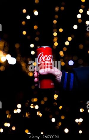 Belgrad, Serbien - 5. Januar 2023: Coca-Cola-Dose in der Hand mit Weihnachtslichtern und Dekorationen im Hintergrund bei Nacht in Belgrad, Serbien Stockfoto