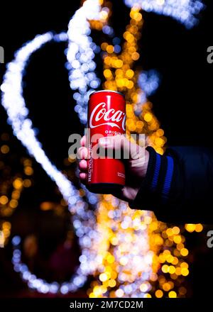 Belgrad, Serbien - 5. Januar 2023: Coca-Cola-Dose in der Hand mit Weihnachtslichtern und Dekorationen im Hintergrund bei Nacht in Belgrad, Serbien Stockfoto